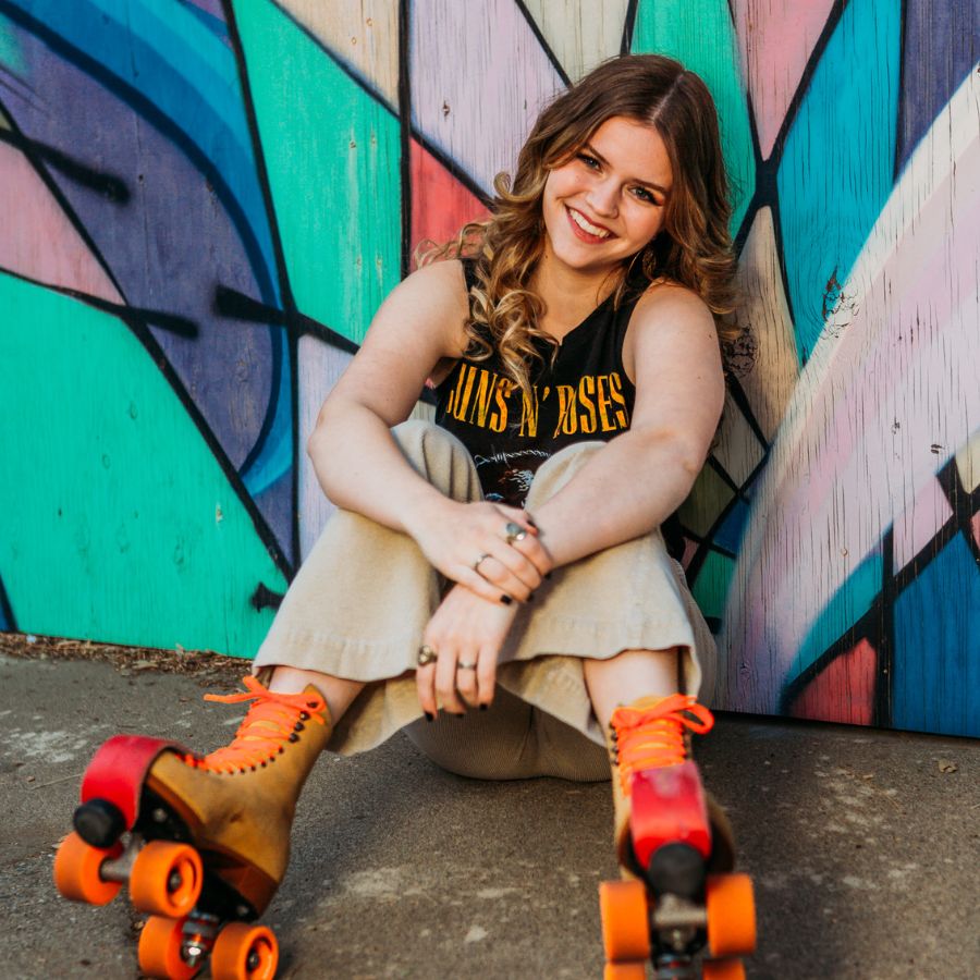 Image of a young woman sitting on the ground wearing rollerskates in from of a graffiti wall